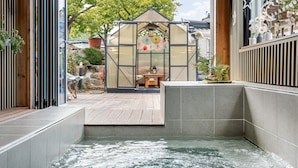 Uma área de spa com hidromassagem, deck de madeira e estrutura de vidro tipo estufa.