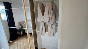A walk-in closet with a mirrored wardrobe, a bed, and a small table with a lamp.