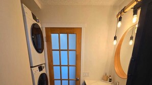 A compact bathroom with a wooden floor, a large mirror, a sink, and a washing machine.