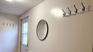 Un couloir avec une porte blanche, une fenêtre, un porte-manteau et un miroir au mur.