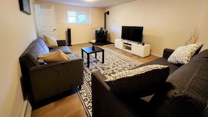 Un salon avec un canapé, une table basse, un téléviseur posé sur un meuble et un tapis à motifs.