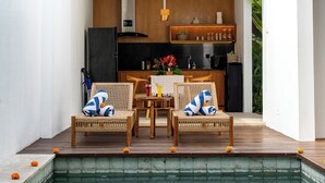 A poolside area with wicker chairs, a dining table, and a kitchen in the background. - Silk Umalas by Nagisa Bali (Kerobokan)