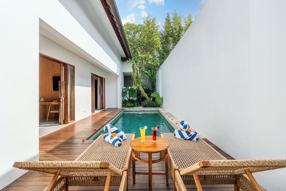 Zona de piscina con terraza de madera, mobiliario de mimbre y vistas al verdor.