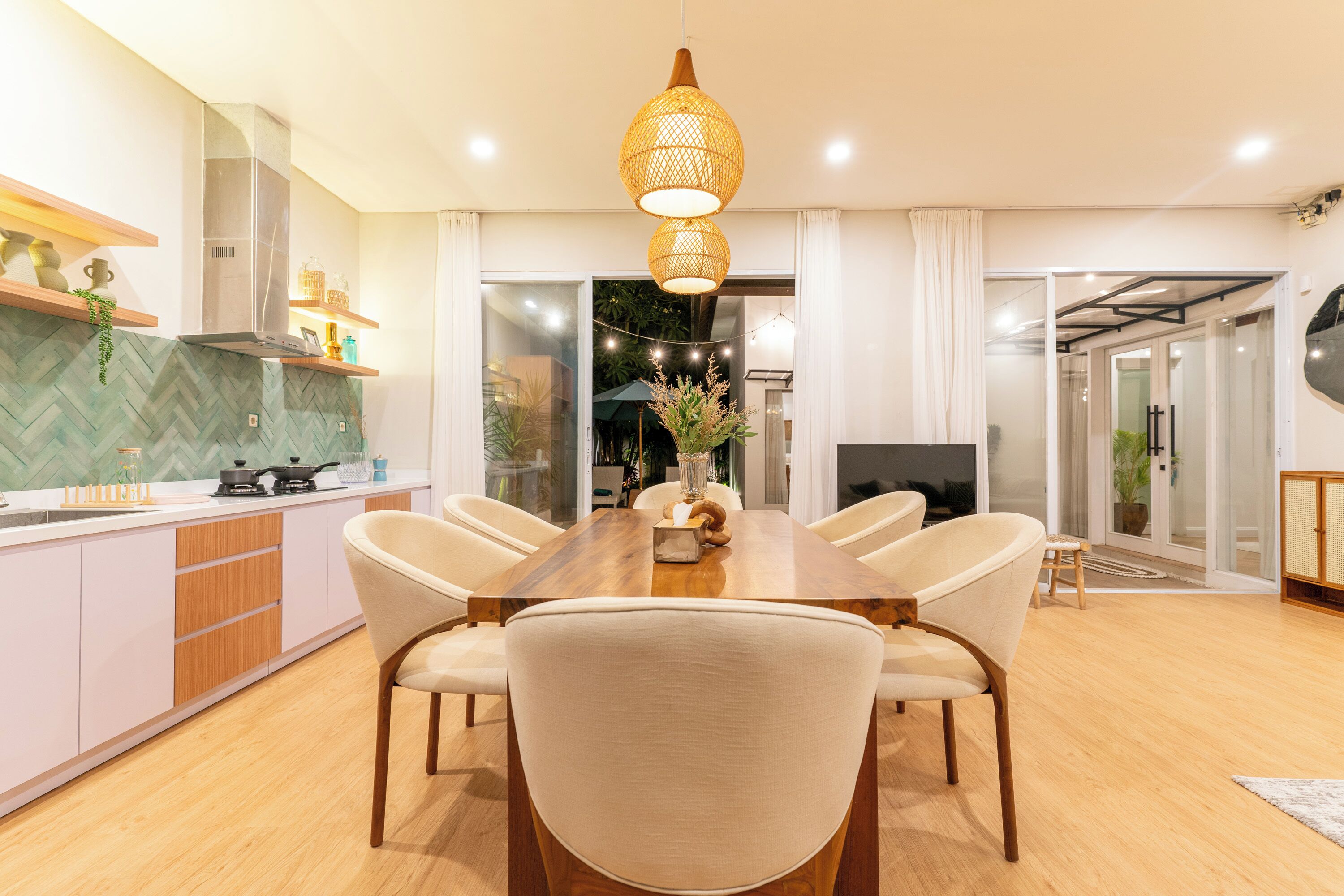 A modern kitchen with a dining area, featuring a wooden table, chairs, and a hanging light fixture.