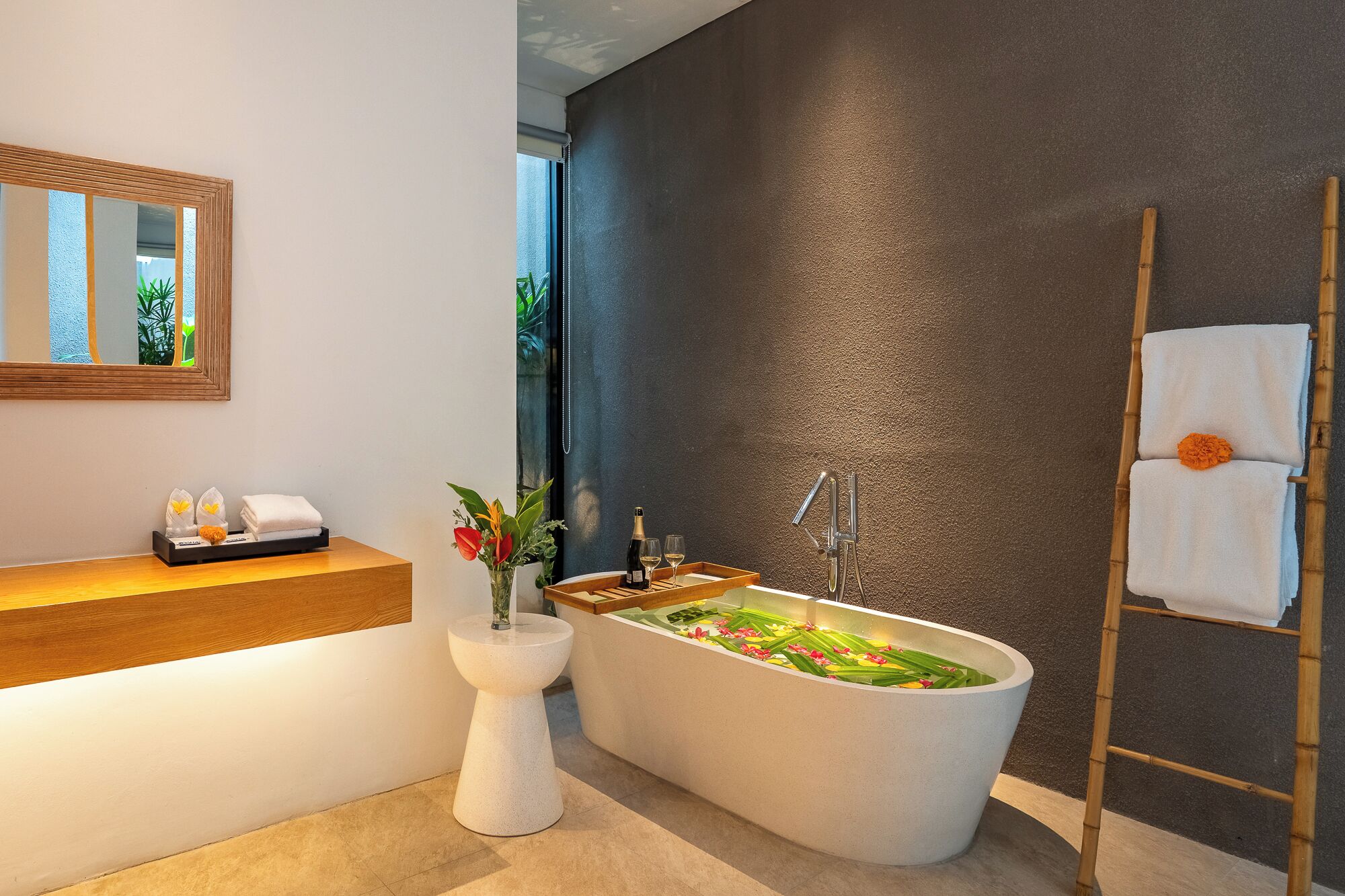 Un baño moderno con una bañera independiente, un tocador de madera, un espejo grande y un perchero para toallas.