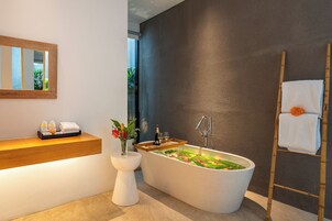 Un baño moderno con una bañera independiente, un tocador de madera, un espejo grande y un perchero para toallas.