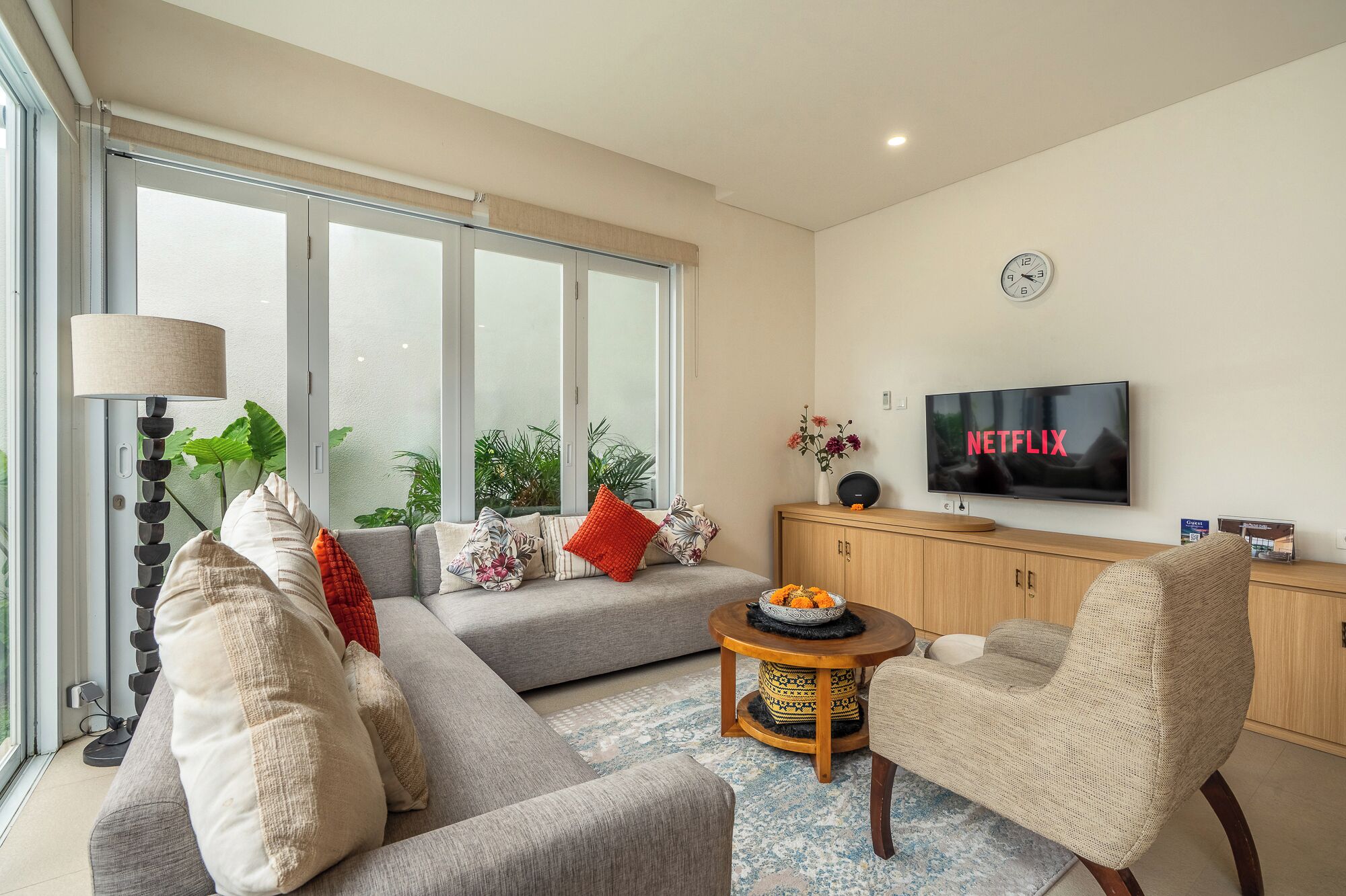 A modern living room with a sofa, armchairs, a coffee table, a TV, and a large window.