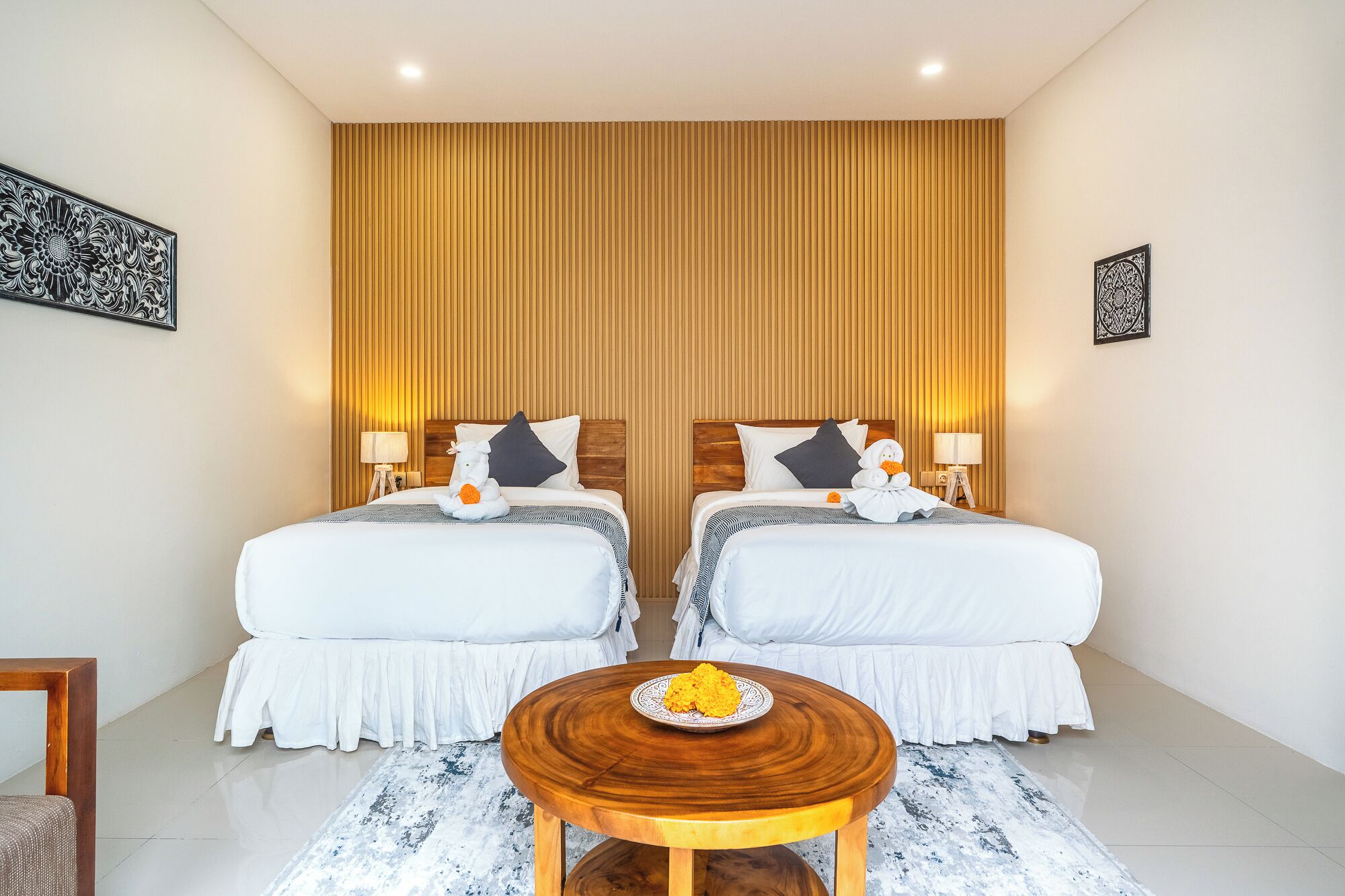 A hotel room with two beds, a round wooden table, and a decorative wall panel.