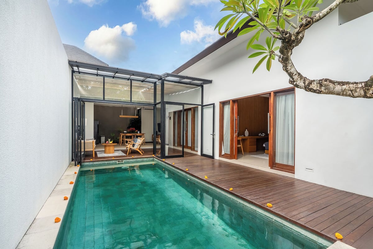 Una casa moderna con piscina, terraza de madera y puertas de cristal que dan a una sala de estar.