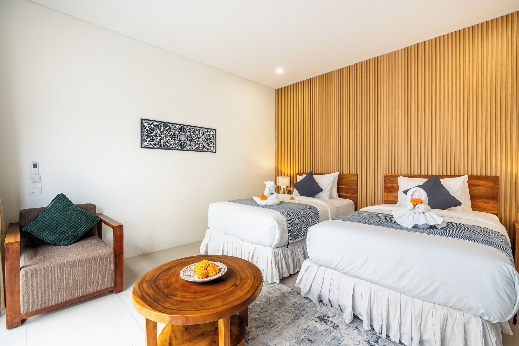 Habitación de hotel con dos camas, un panel de pared de madera, una mesita con un plato de fruta y una silla con cojín verde.