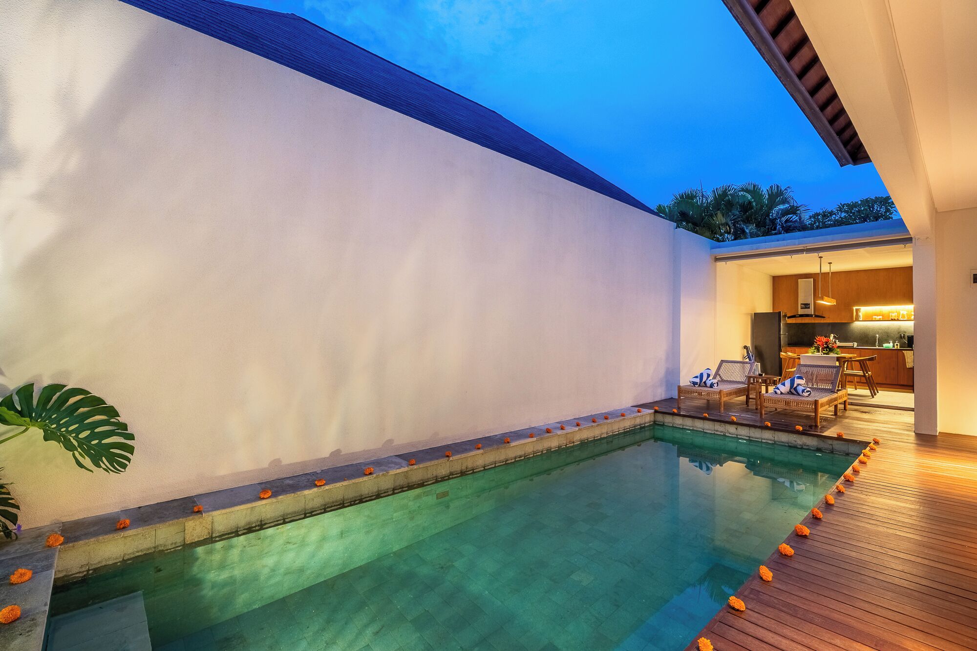 Une piscine avec une terrasse en bois, un coin cuisine et un espace salon avec des chaises.