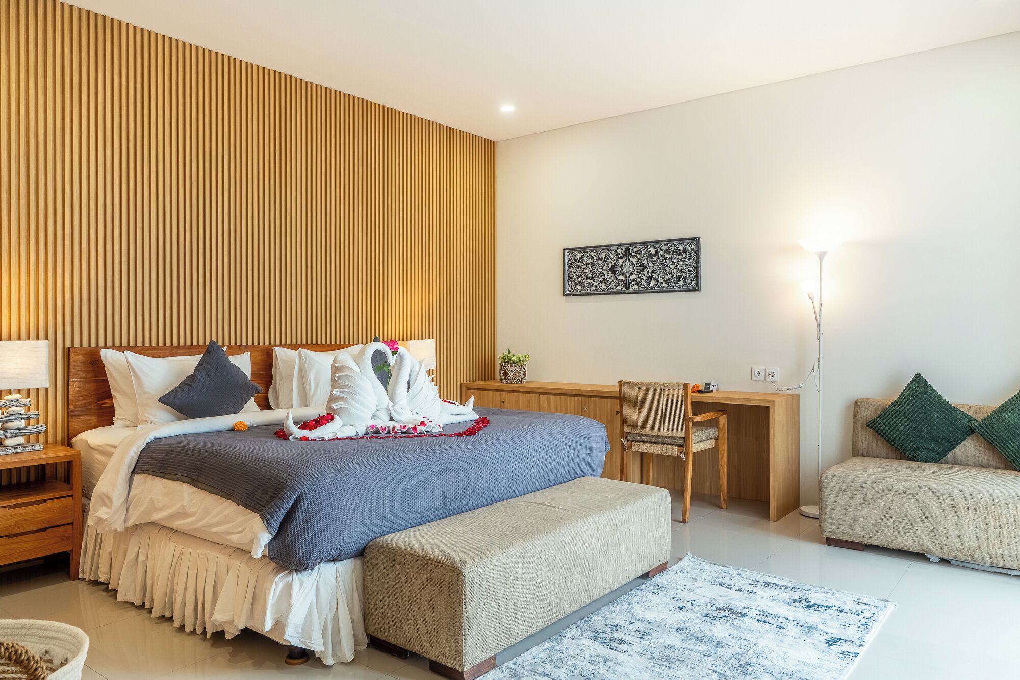 A modern hotel room with a bed, bedside table, chair, desk, and a lamp.
