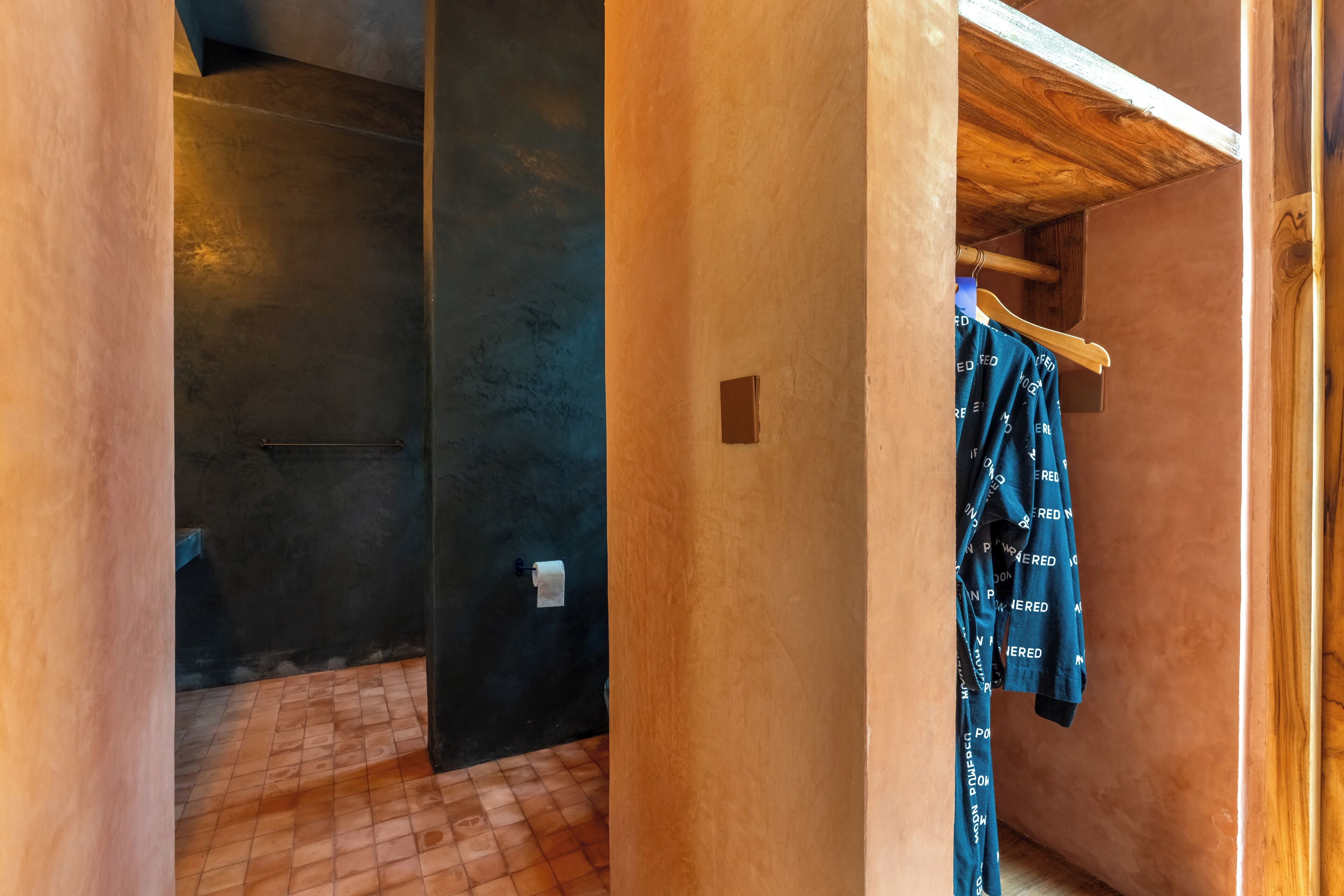 A room with a tiled floor, a wooden beam ceiling, and a hanging garment rack with clothes.