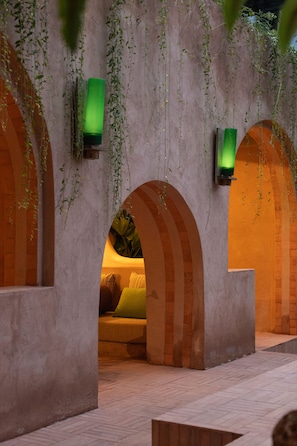 Un pasillo con arcos, luces verdes empotradas en la pared y enredaderas colgantes.