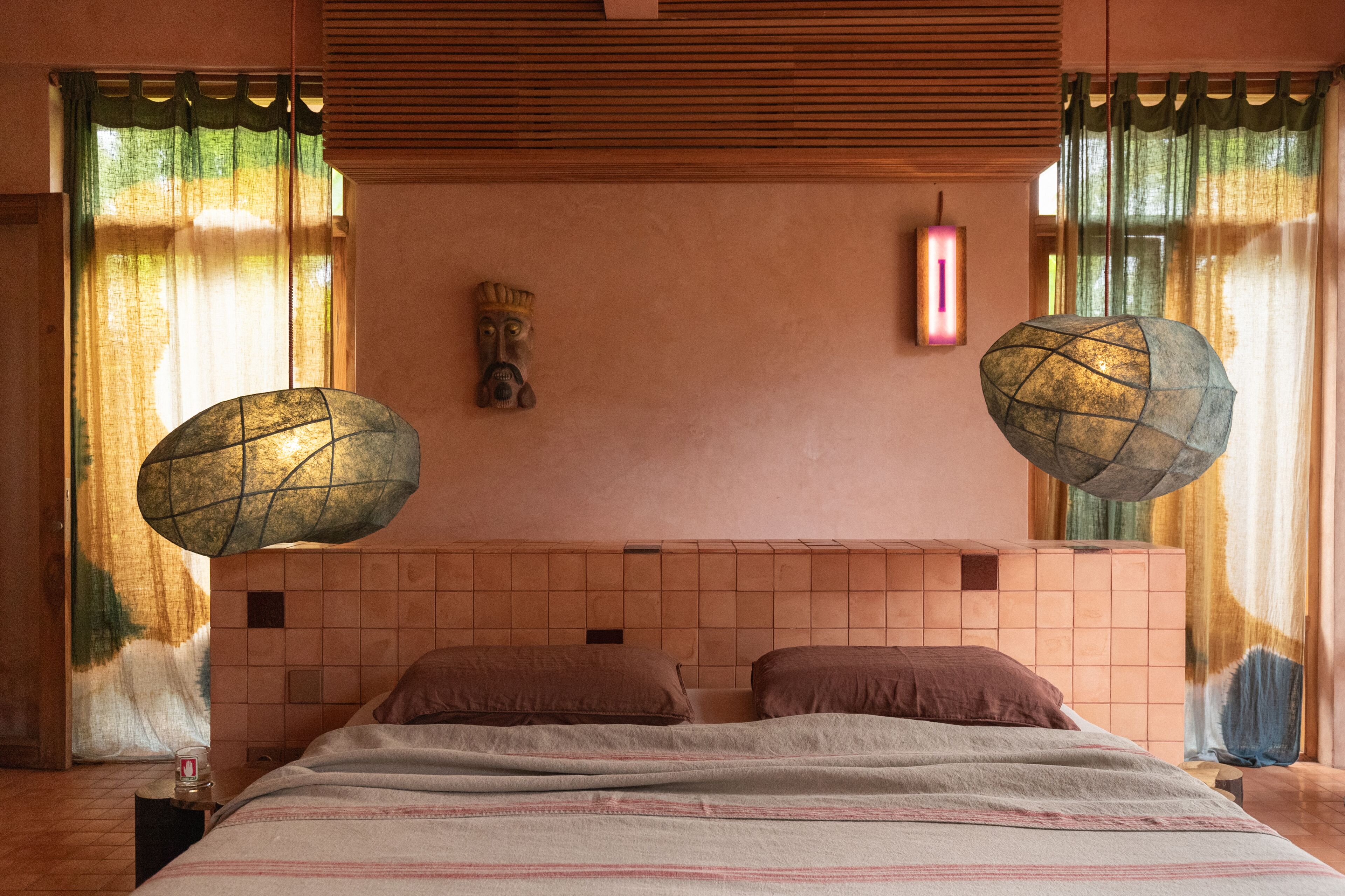 A bedroom with a large bed, two pillows, a nightstand, a wall-mounted light, and a decorative wall piece.
