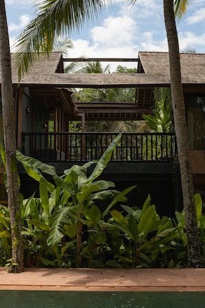 Un edificio de dos pisos con un balcón, rodeado de vegetación tropical.