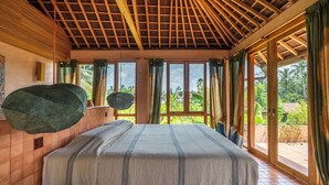 Un dormitorio con una cama grande, vigas de madera en el techo y vistas al verde exterior.
