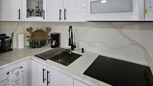 A kitchen with white cabinets, a microwave, a sink, and a coffee maker. - Kick back and relax in this calm, stylish space. (Ponce)