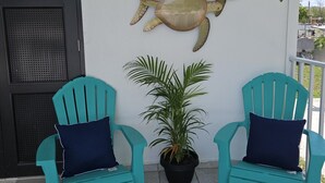 Two turquoise chairs with dark cushions, a potted plant, and two turtle wall art pieces on a balcony with a tiled floor. - Kick back and relax in this calm, stylish space. (Ponce)