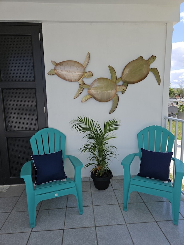 Two turquoise chairs with dark cushions, a potted plant, and two turtle wall art pieces on a balcony with a tiled floor. - Kick back and relax in this calm, stylish space. (Ponce)