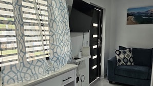 A modern living room with a white desk, a blue sofa, and a flat-screen TV mounted on the wall. - Kick back and relax in this calm, stylish space. (Ponce)