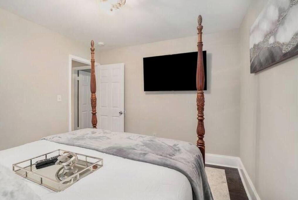 A bedroom with a four-poster bed, a flat-screen TV mounted on the wall, and a door leading to another room.