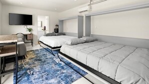 Una camera da letto moderna con un letto, una scrivania, una sedia, una televisione e un'ampia finestra.
