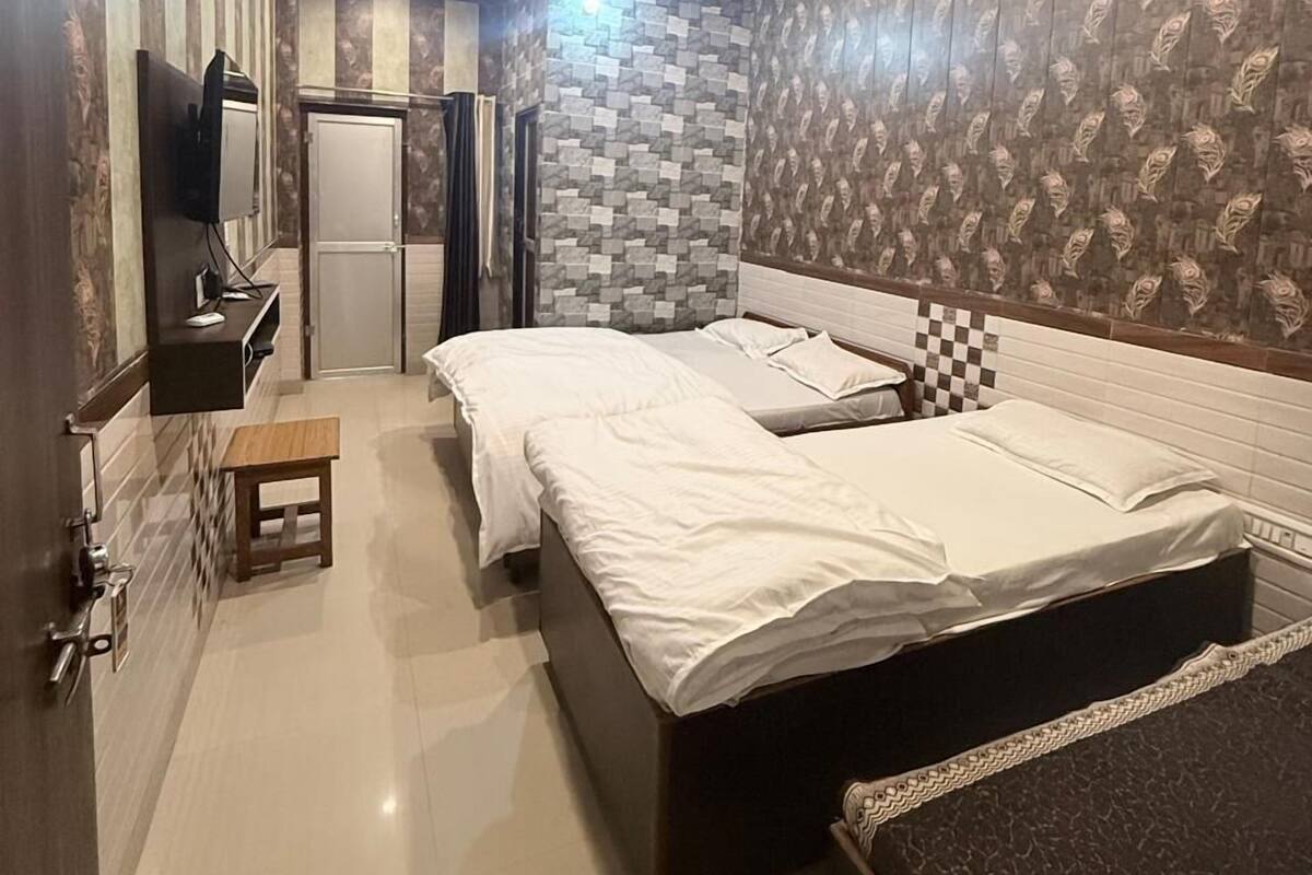A bedroom with two beds, a small table, a TV, and a bathroom with patterned wallpaper.