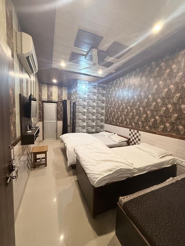 A bedroom with two beds, a small table, a TV, and a bathroom with patterned wallpaper. - Hotel Aapno Shyam And Restaurant (Danta Ramgarh)