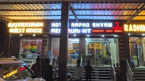 Un hotel y restaurante con letreros de neón que indican "HOTEL", "HABITACIONES CON Y SIN AIRE ACONDICIONADO" y "AAPNO SHYAM RESTAURANT".