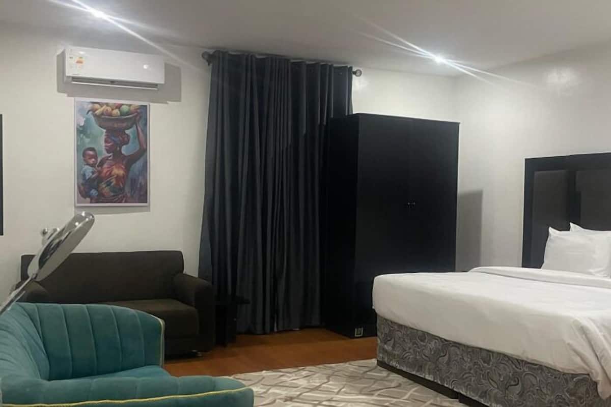 Una habitación de hotel con una cama, un sofá, una silla, un cuadro en la pared y una cortina.