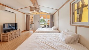Habitación de hotel con televisor, dos camas, techo de madera y vistas al exterior.