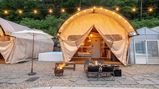 A cozy outdoor tent with a fire pit and dining setup, surrounded by string lights and a stone-paved area. - Mungyeong The Most Glamping (Mungyeong)