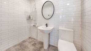 A bathroom with white subway tiles, a white sink, a toilet, and a mirror.