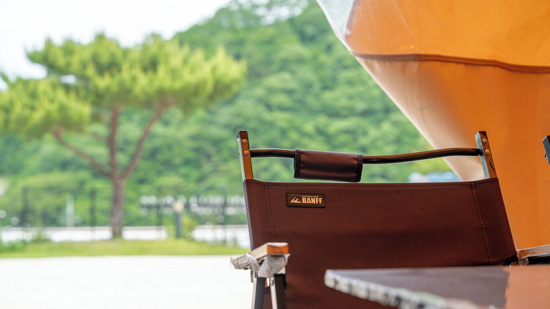 A brown outdoor camping chair with a metal frame and a 'Outdoor Camp Banff' label, positioned near a grill.