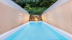A rectangular pool with a clear blue water surface, surrounded by beige walls, with a stone wall and greenery in the background. - Mungyeong The Most Glamping (Mungyeong)