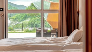 A hotel room with a bed, a window with a view of a green landscape, and a lamp.