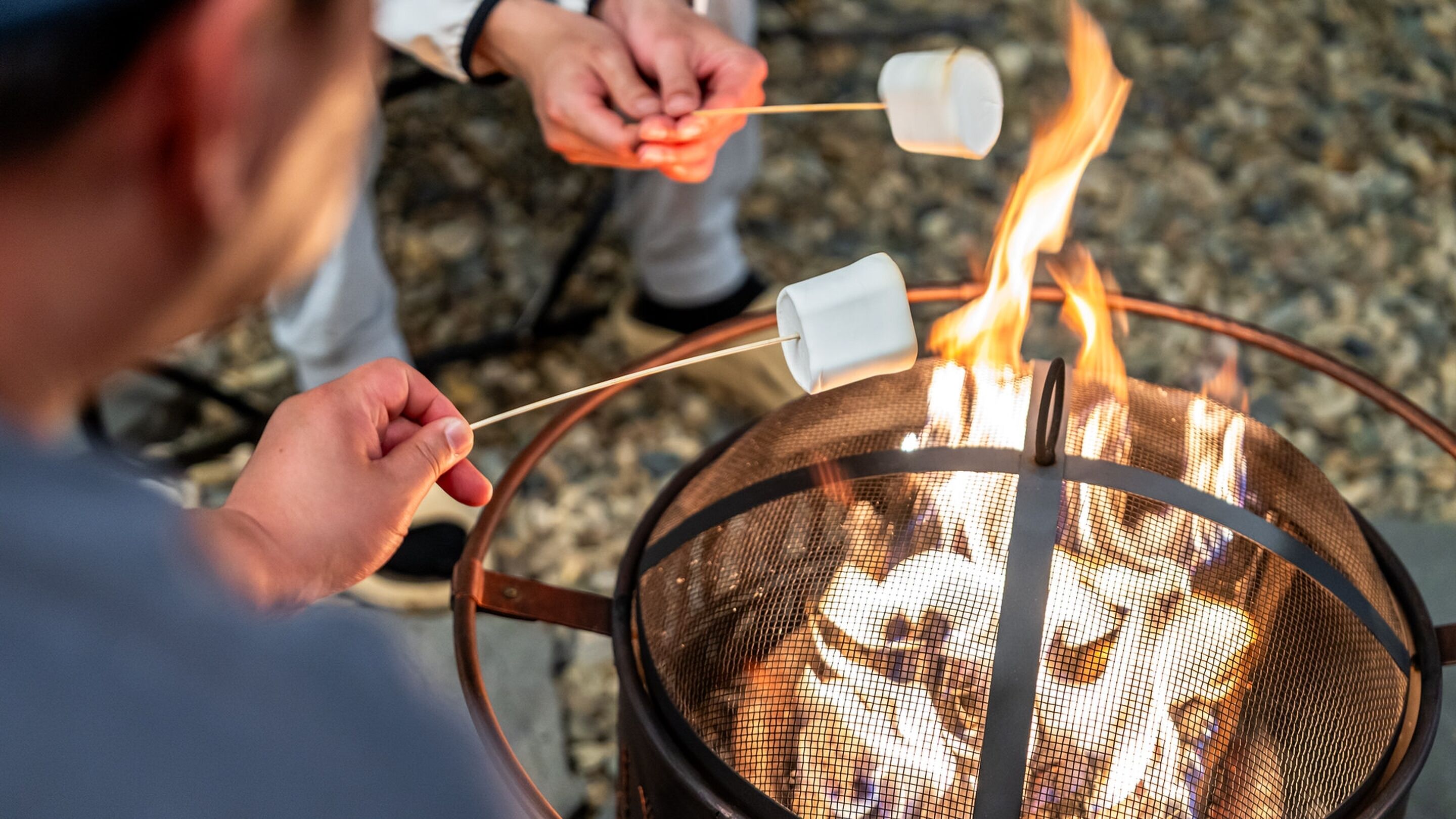 Una persona asando malvaviscos sobre un pozo de fuego al aire libre.