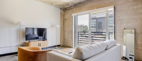 Relax in this stylish living room with a large flat-screen TV, comfortable sofa, and balcony access to city views.