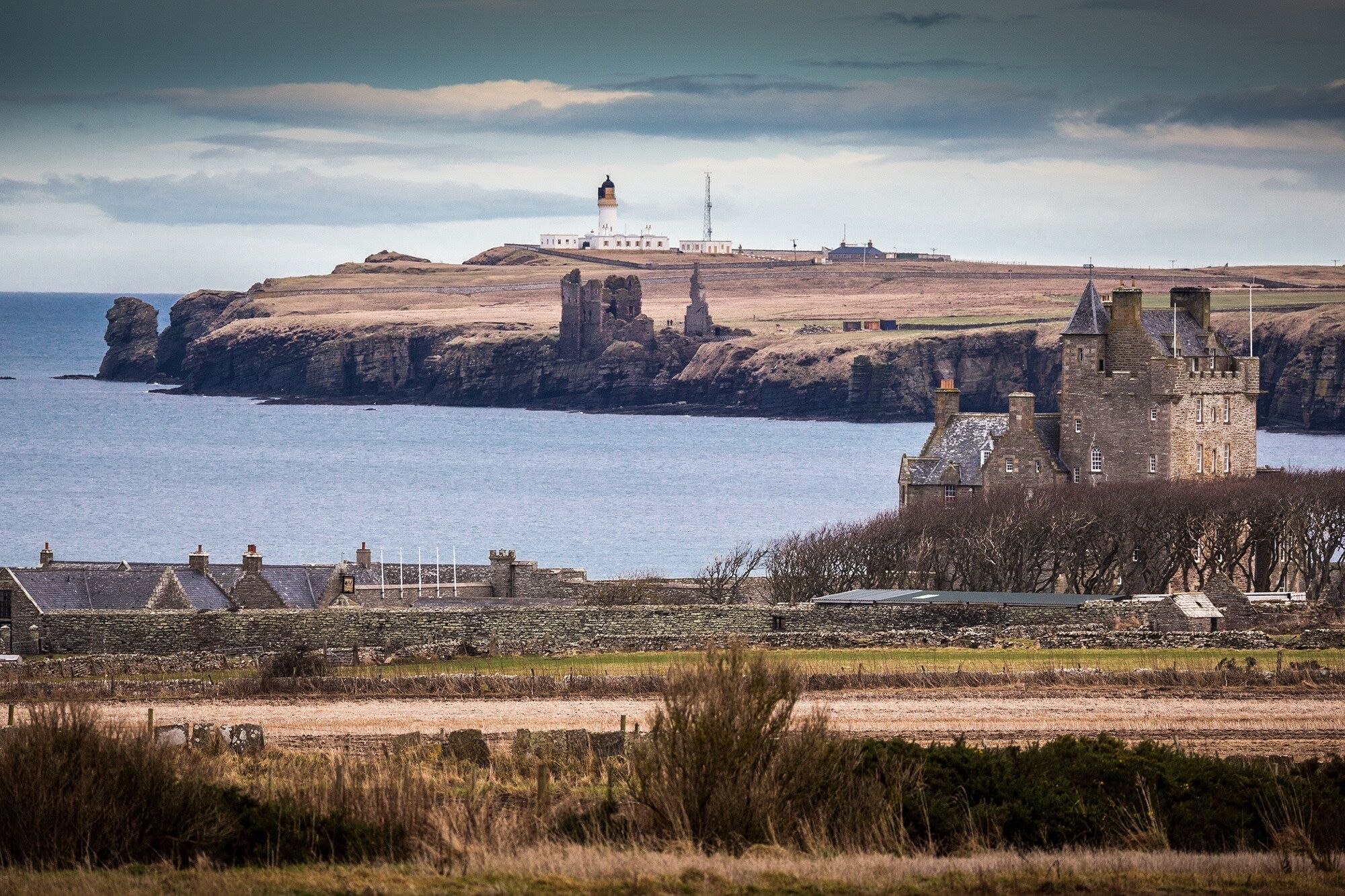 Eine Küstenlandschaft mit Burg, Leuchtturm und Steinmauer.