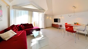 A modern living room with a red sofa, a glass coffee table, and a dining area with red chairs.