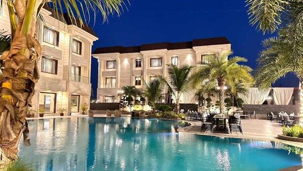 A hotel pool area with a large pool, palm trees, and outdoor seating. - The Imperial Prime (Bhilwara)