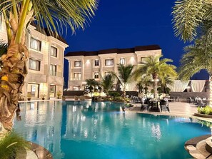 A hotel pool area with a large pool, palm trees, and outdoor seating. - The Imperial Prime (Bhilwara)