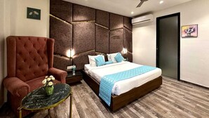A modern hotel room with a large bed, a red armchair, a small round table, and a ceiling fan. - The Imperial Prime (Bhilwara)