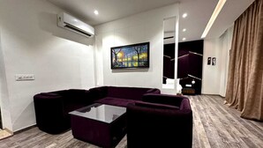 A modern living room with a sectional sofa, a glass coffee table, and a painting on the wall. - The Imperial Prime (Bhilwara)