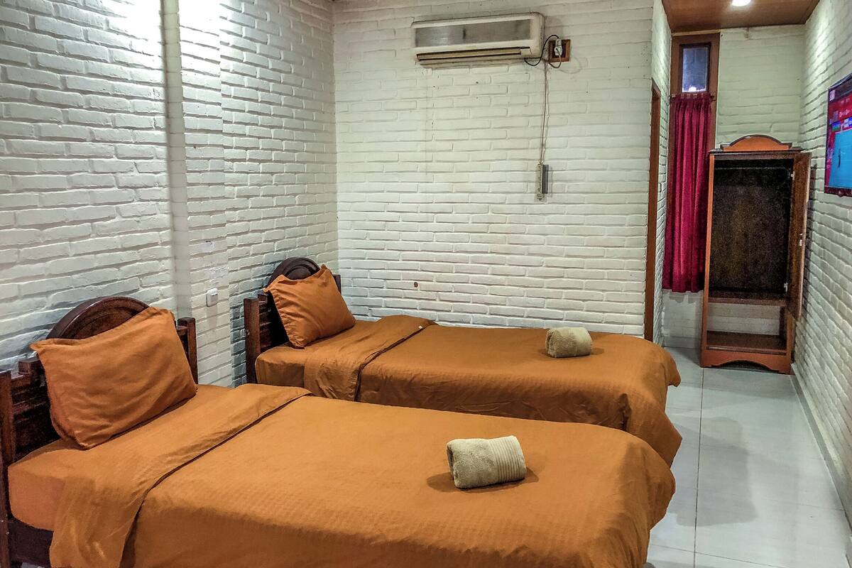 Une chambre avec deux lits, des murs en briques blanches, un climatiseur et une armoire en bois.