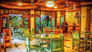 A restaurant with round tables and green chairs, wooden ceiling, and brick walls.