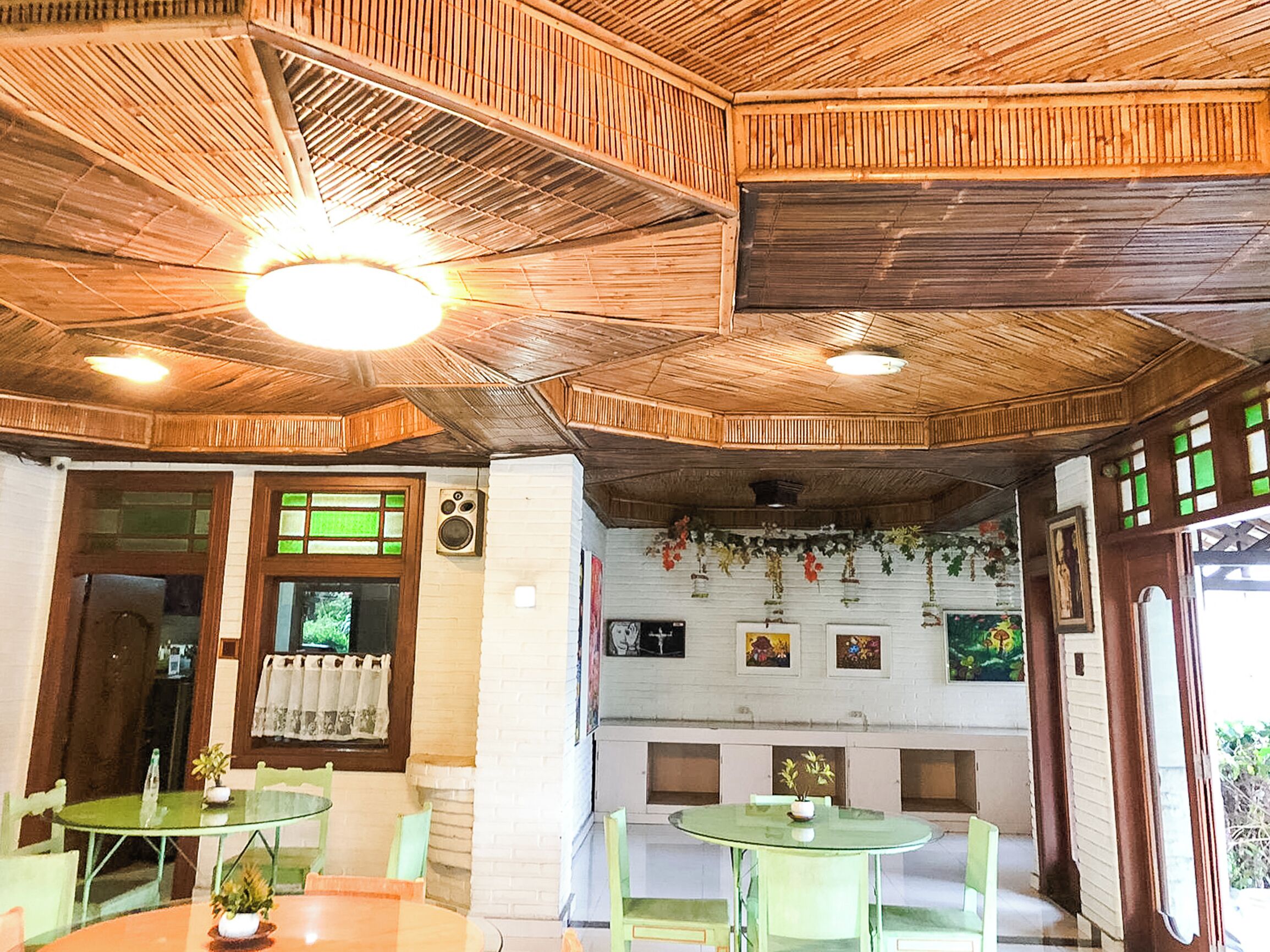 A restaurant with wooden ceiling beams, green glass tables, and white brick walls.