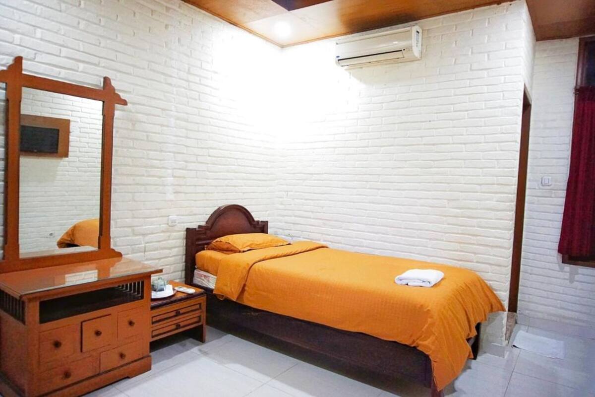 Une chambre avec un lit en bois, une commode, un miroir et un mur en briques blanches.