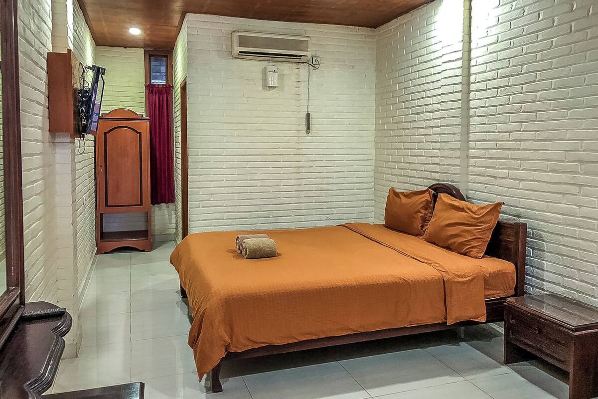 Une pièce avec un lit, une armoire en bois et un mur en briques blanches.